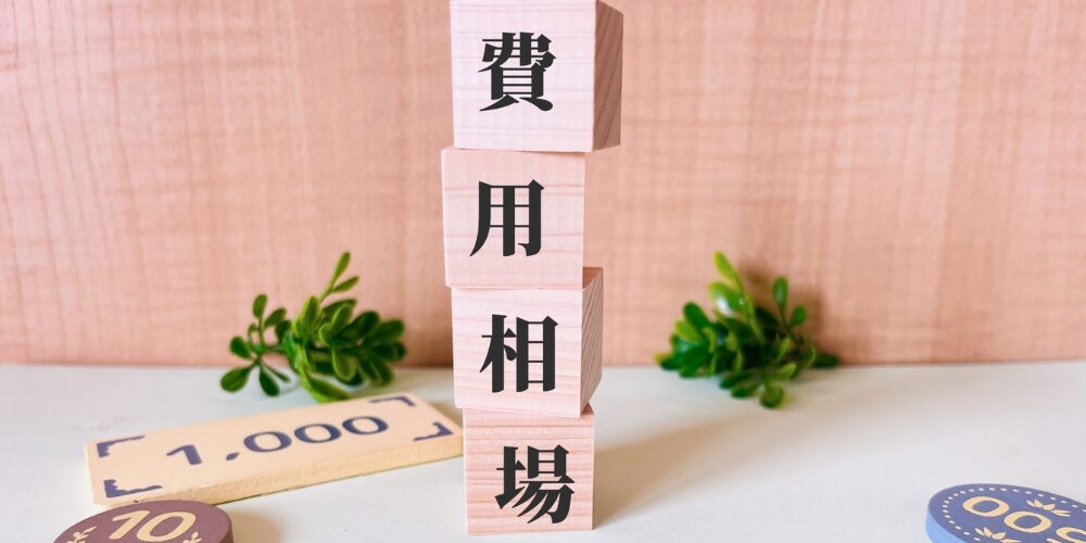 「費用相場」と書かれた積み木と1,000円のプレート、観葉植物が添えられたイメージ。