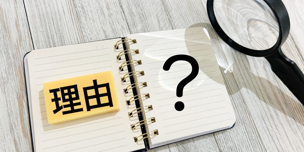リング式ノートに黄色い付箋で『理由』と書かれ、その隣に大きな黒い疑問符が浮かぶ構図と虫眼鏡