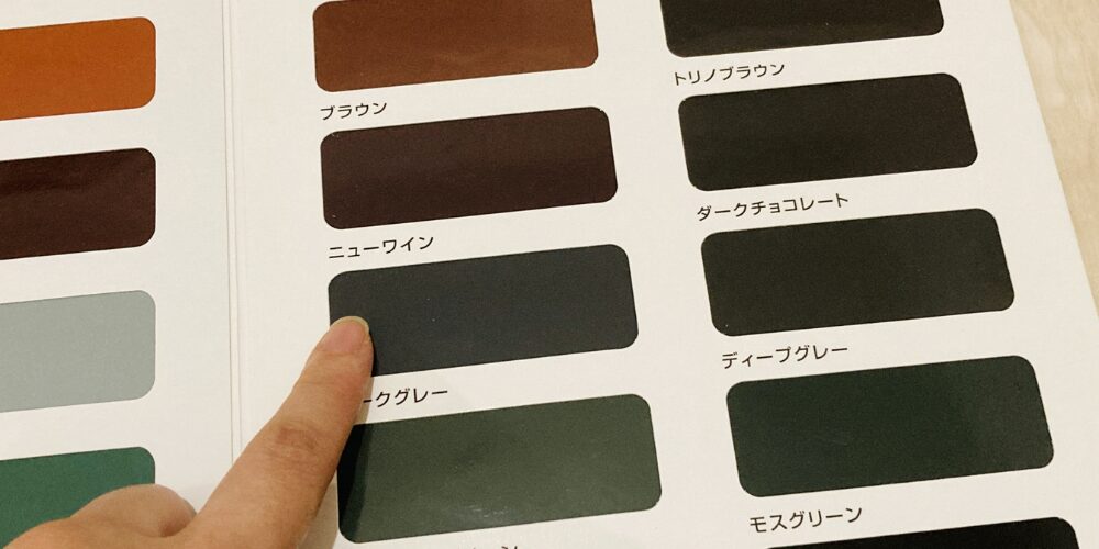 ページに並んだ塗料見本の中で、指が「ライトグレー」を指し示している場面。上段にはブラウン系、下段にはグリーン系の見本が並んでいます。