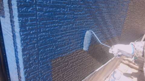 青い塗料で外壁を塗装している手元