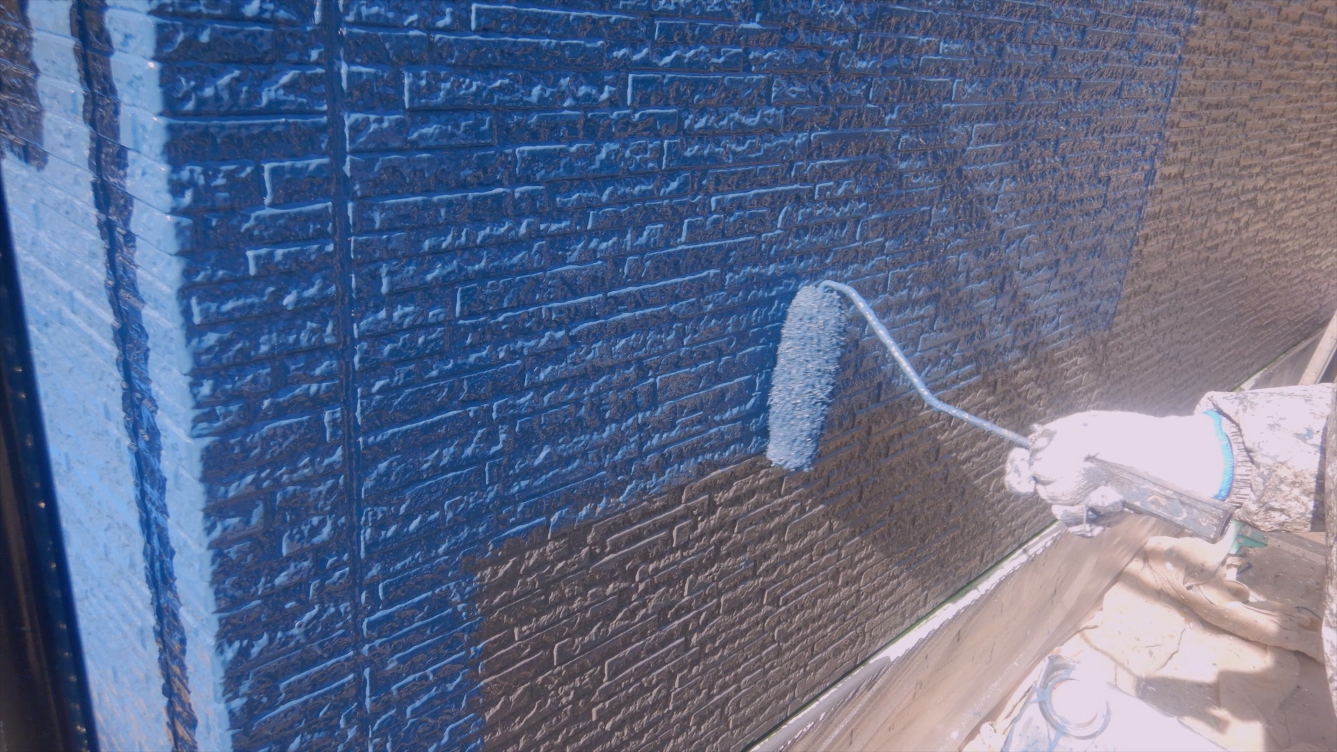 青い塗料で外壁を塗装している手元