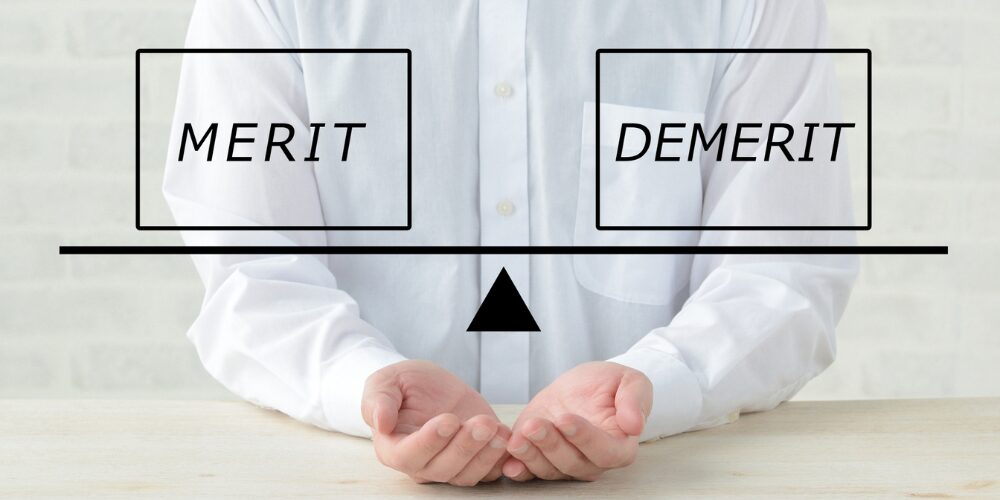 「MERIT」と「DEMERIT」を天秤で比較するビジネスイメージ