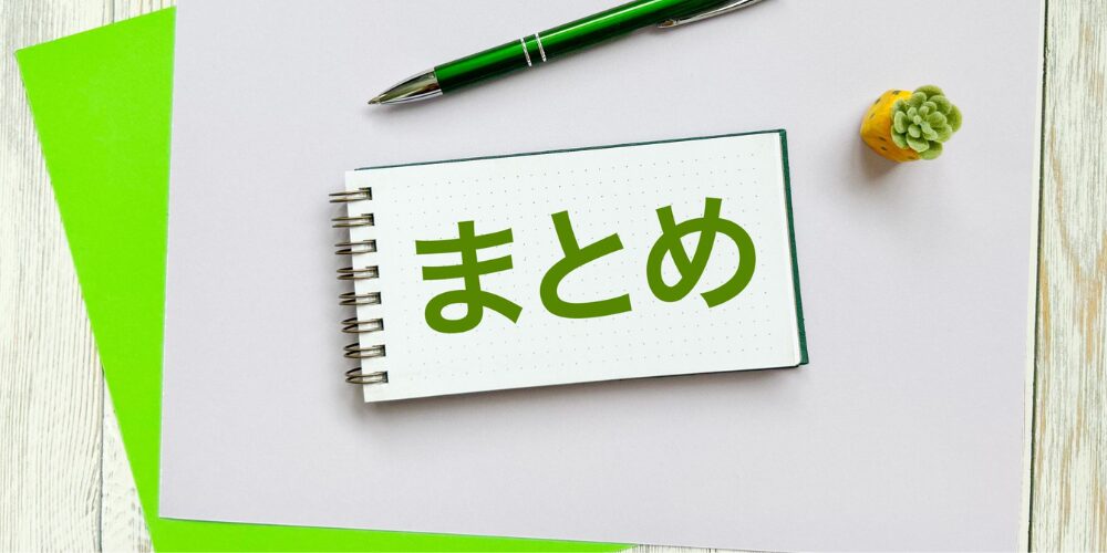白いノートに緑色の文字で『まとめ』と書かれており、隣にペンや多肉植物の飾りが置かれたテーブル上のイメージ